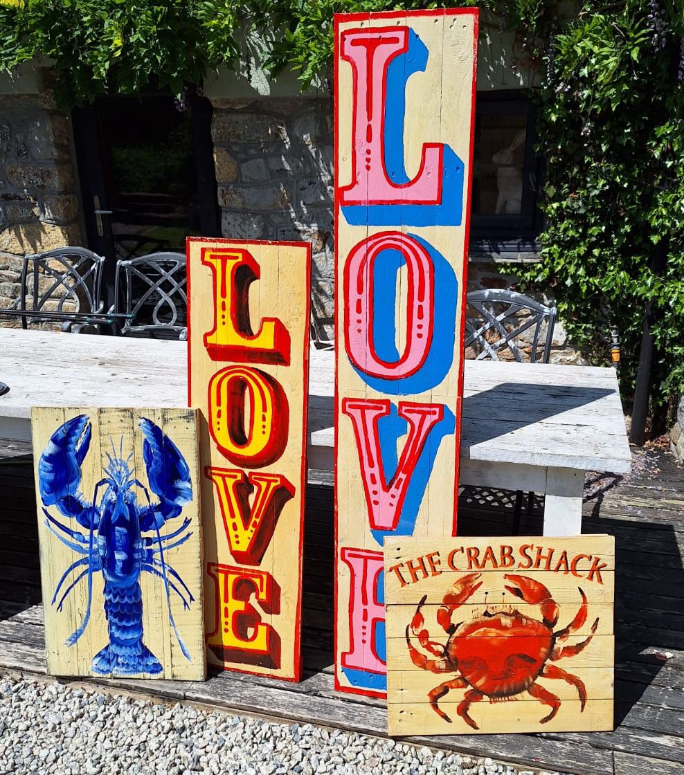 Wooden signs with 'LOVE' and lobster and crab designs outdoors.